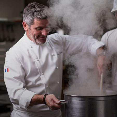 Pâtissier en veste blanche préparant une crème fumante dans une grande casserole