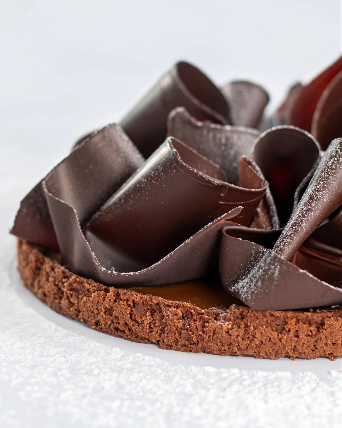 Gros plan d'une tarte au chocolat et caramel avec des copeaux de chocolat et sucre glace.