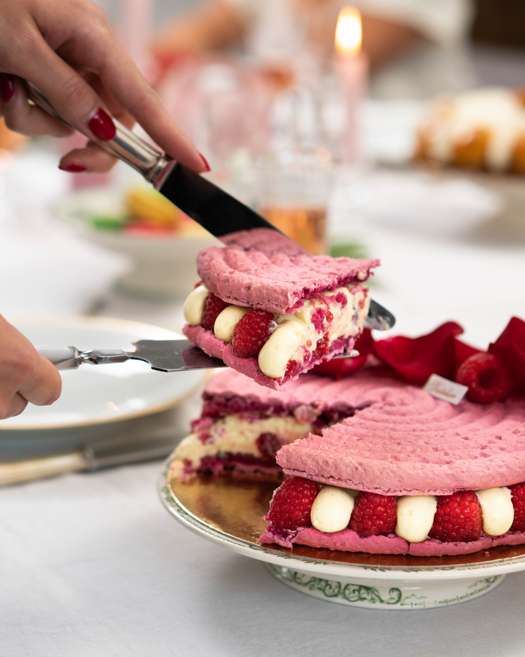 Une main servant une part de gâteau mousse framboise et crème sur un plateau blanc.