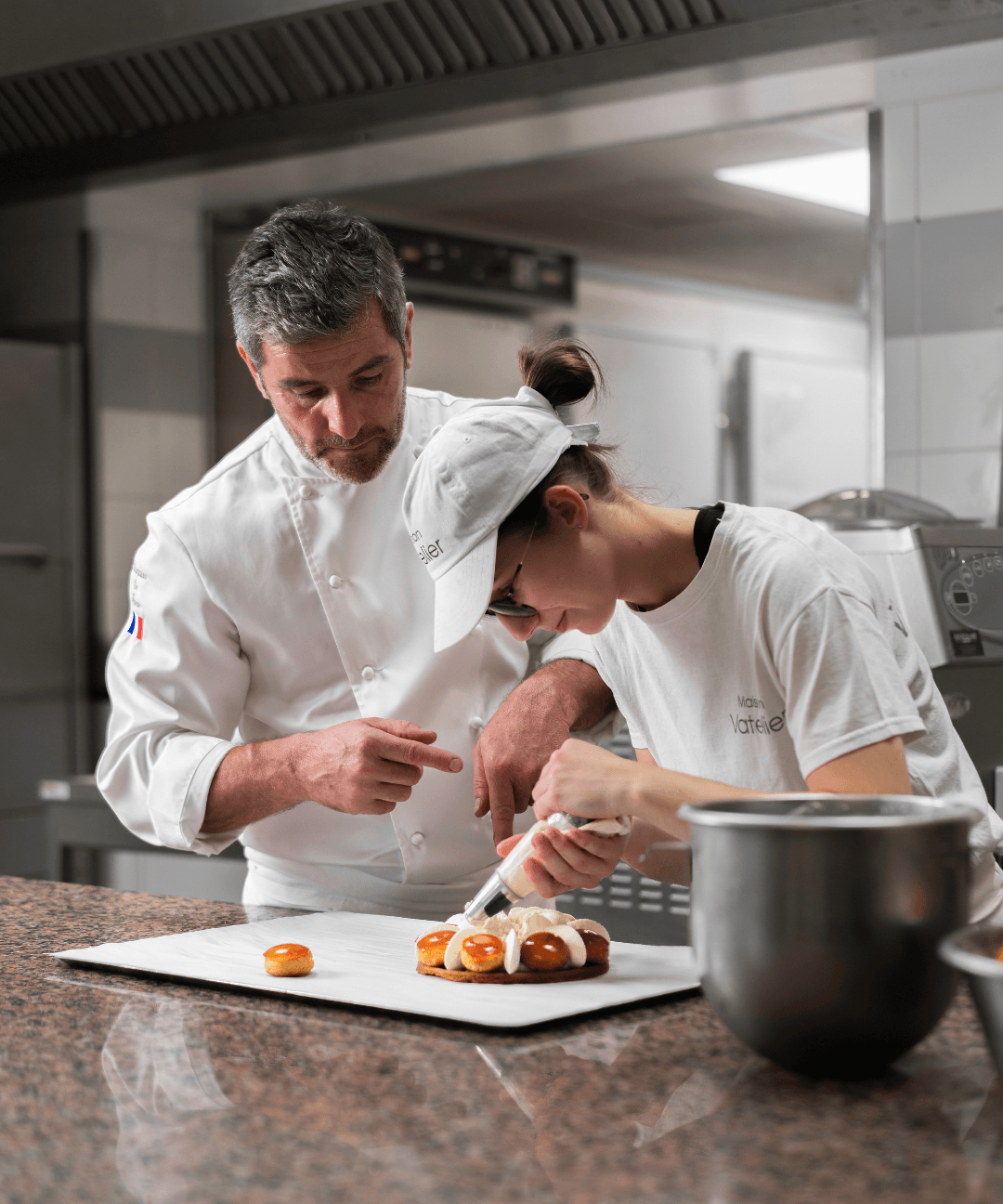Un chef pâtissier et son apprentie préparant un gâteau avec une poche à douille.