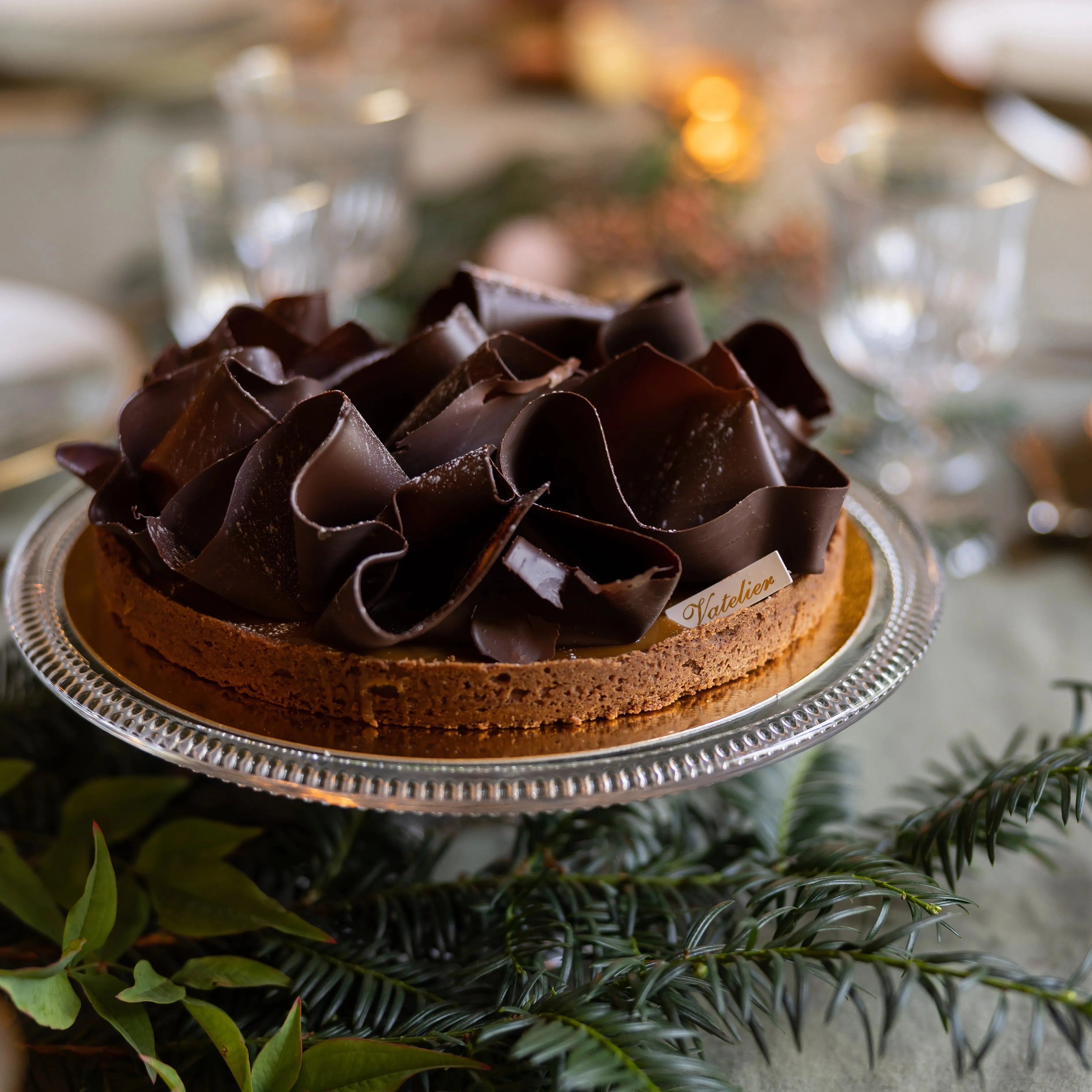 Tarte au chocolat décorée de volutes de chocolat noir sur un plateau en verre.