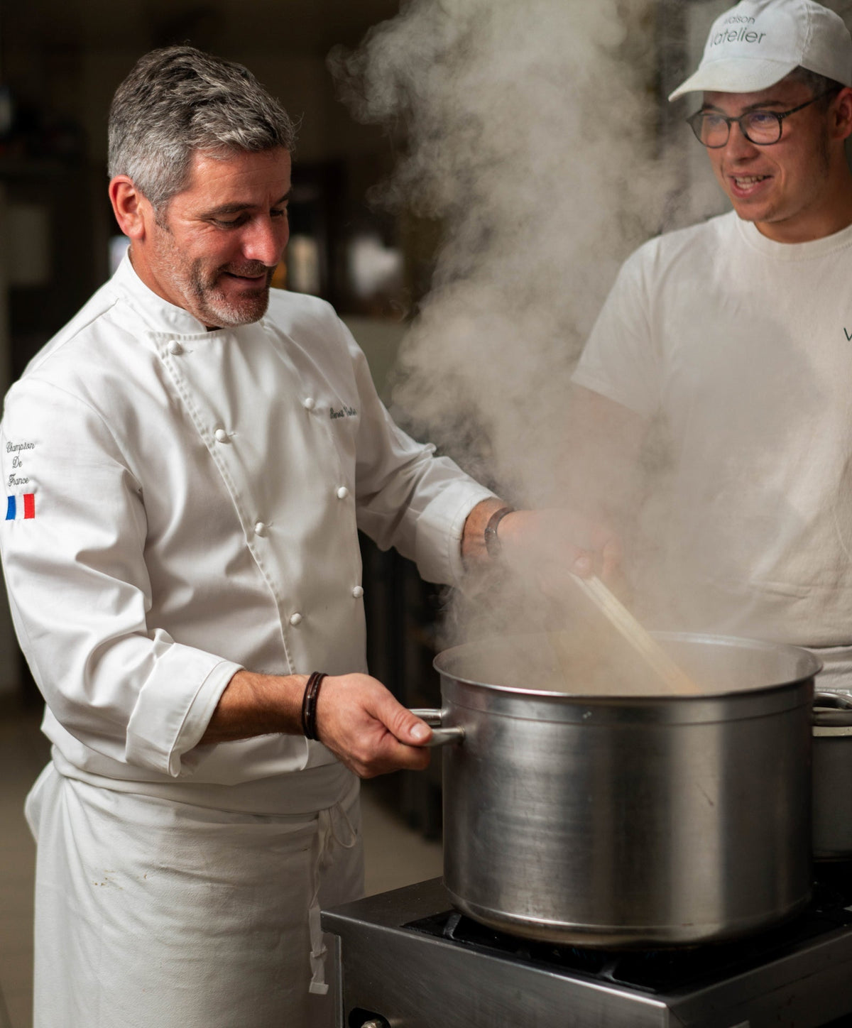 Pâtissier Benoît Vatelier préparant une recette fumante dans une casserole en cuisine.