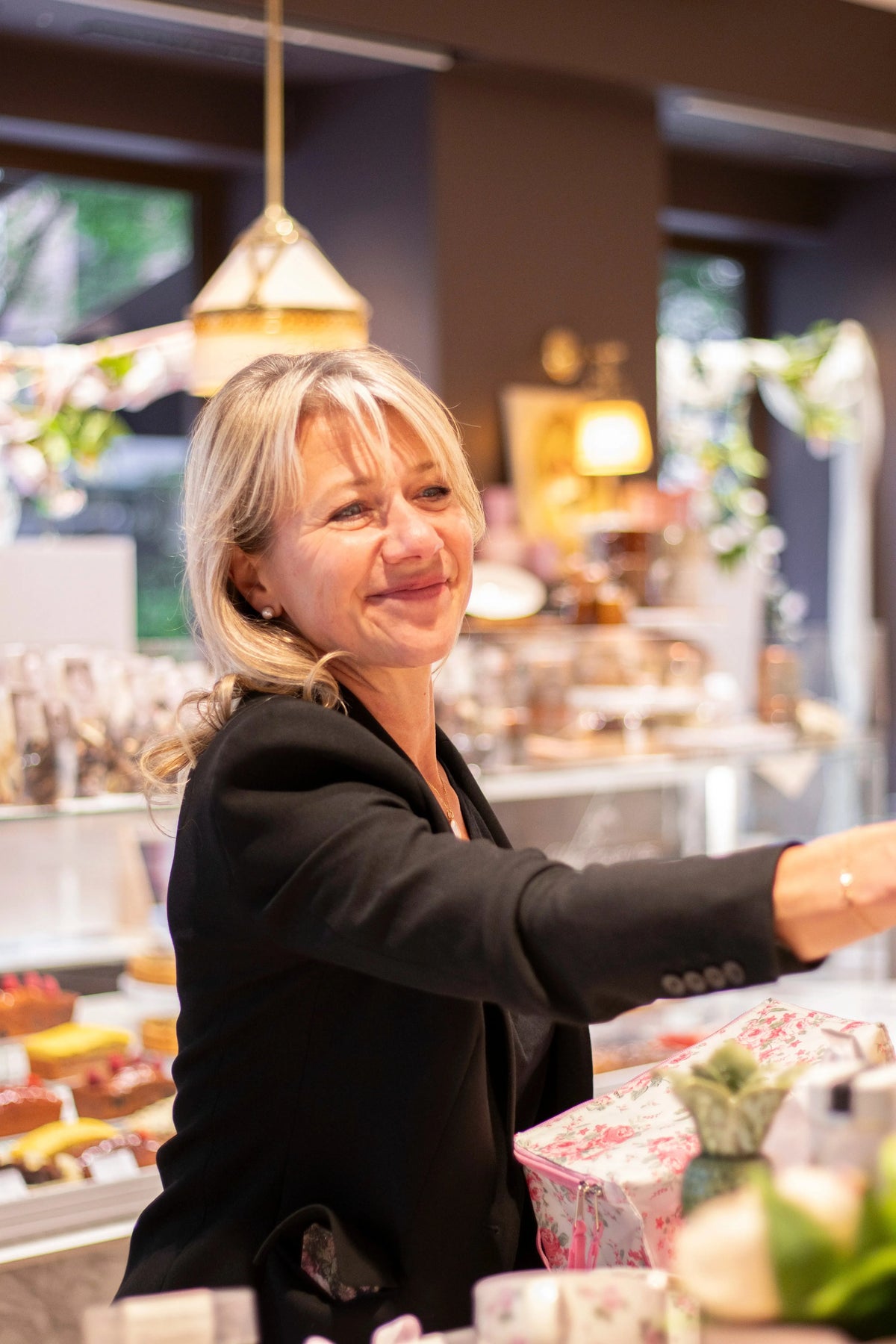 Femme souriante en veste noire servant des pâtisseries dans une boutique.