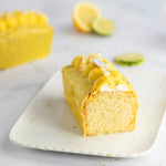 Tranche de cake au citron Maison Vatelier avec glaçage jaune et zestes sur assiette blanche.