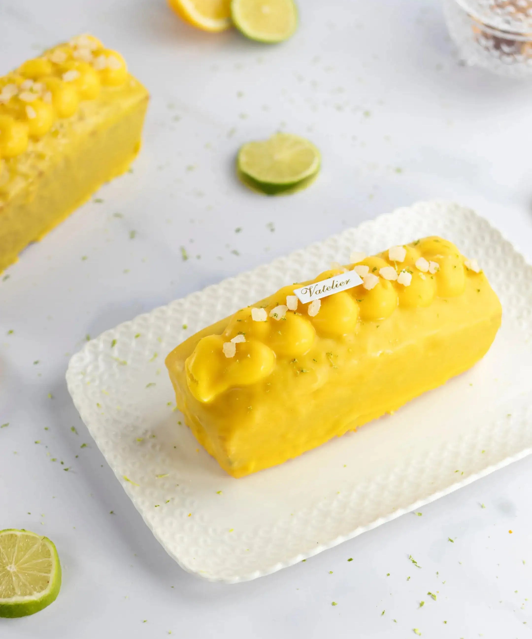 Cake au citron Maison Vatelier avec glaçage jaune et éclats de sel sur plateau blanc.