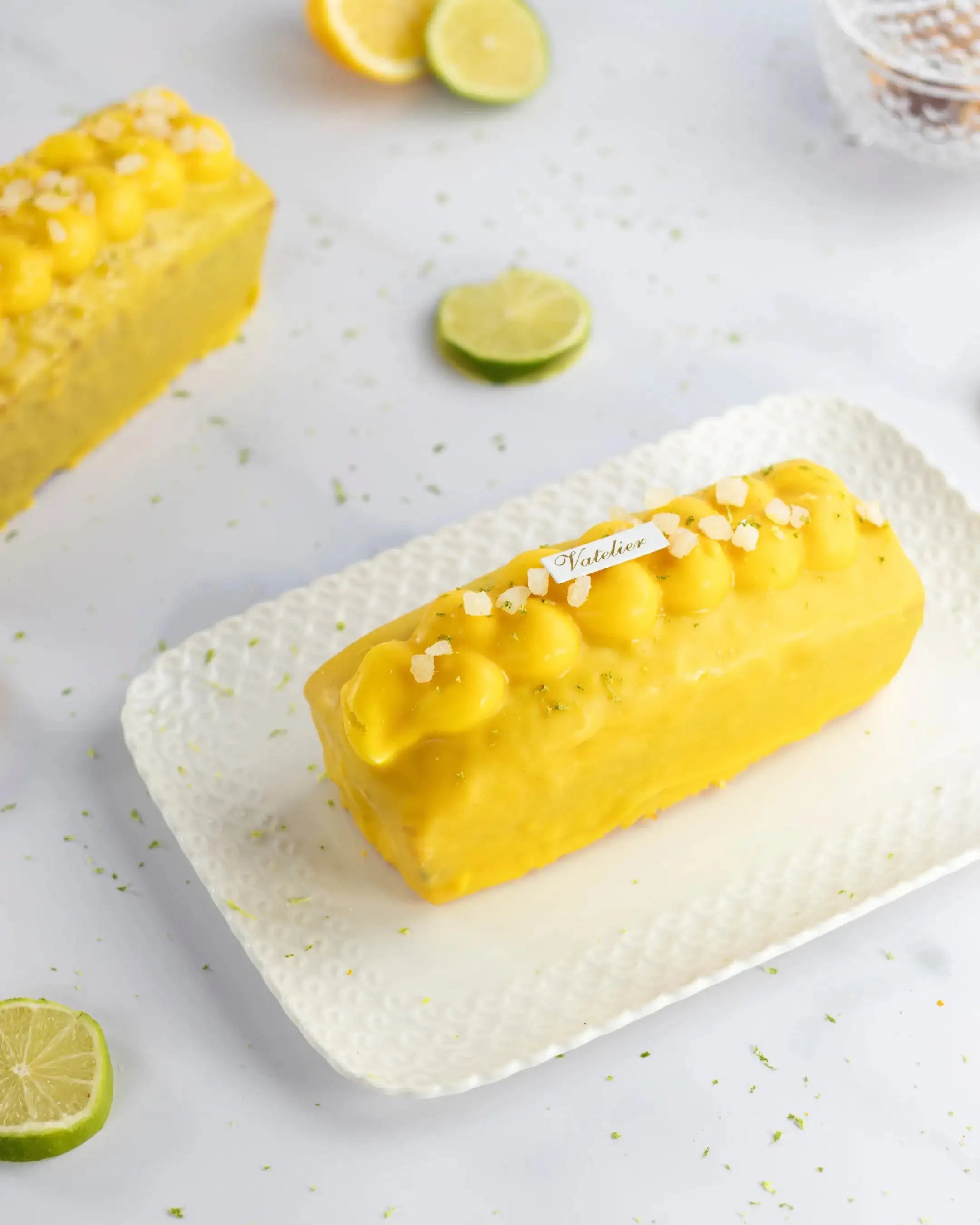 Cake au citron Maison Vatelier avec glaçage jaune et éclats de sel sur plateau blanc.