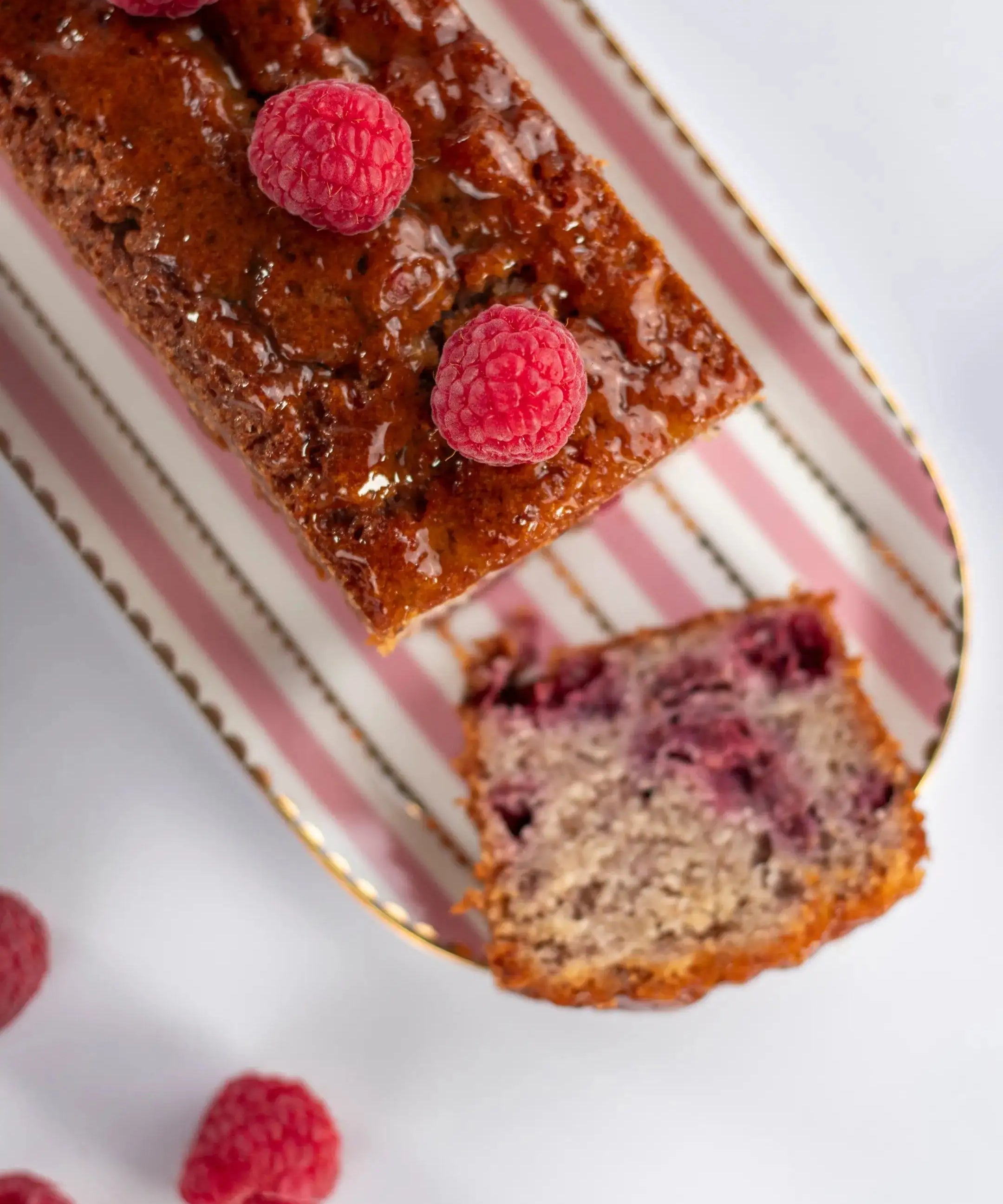 Cake framboise noisette Maison Vatelier avec framboises fraîches sur un plat rayé.