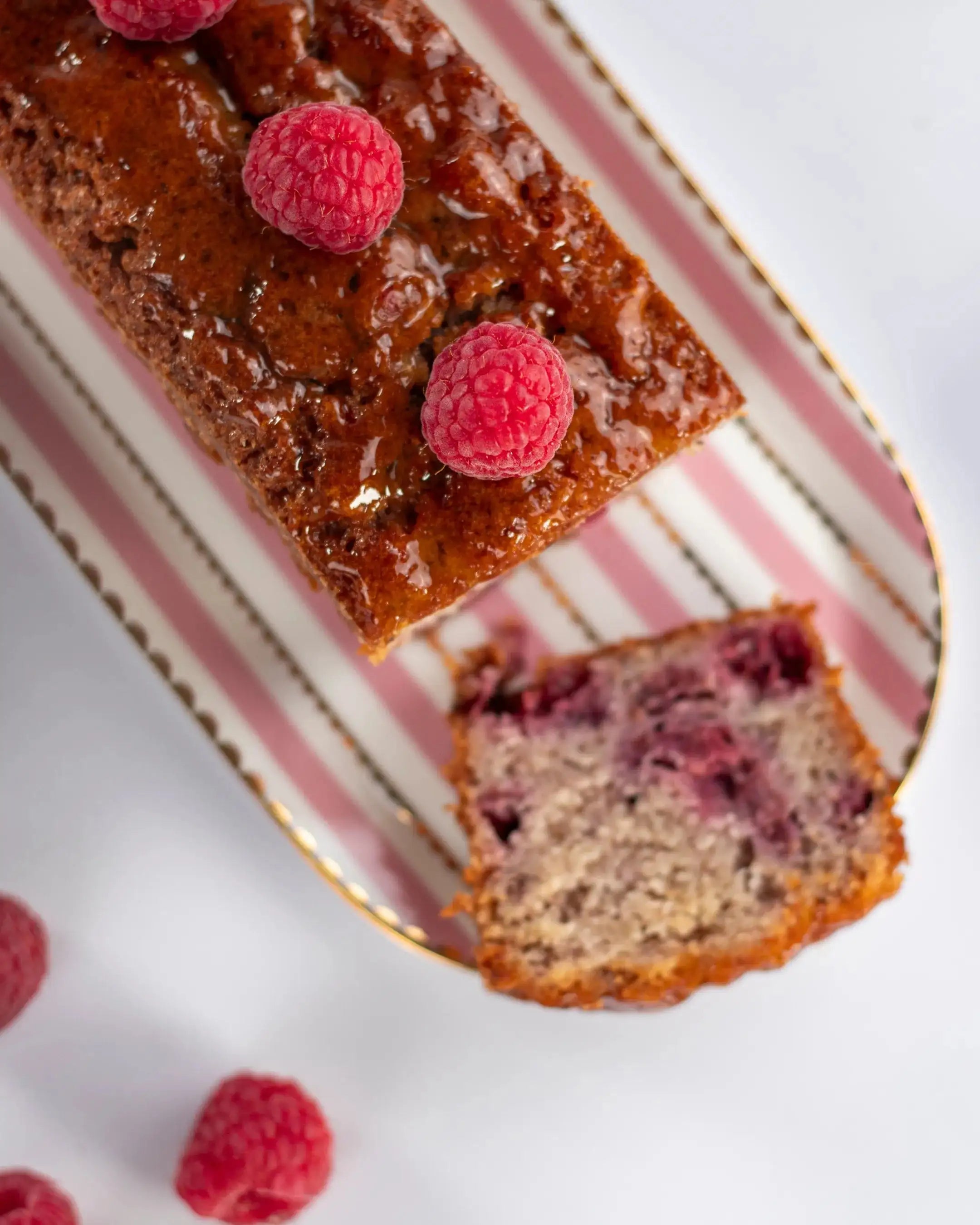 Cake framboise noisette Maison Vatelier avec framboises fraîches sur un plat rayé.