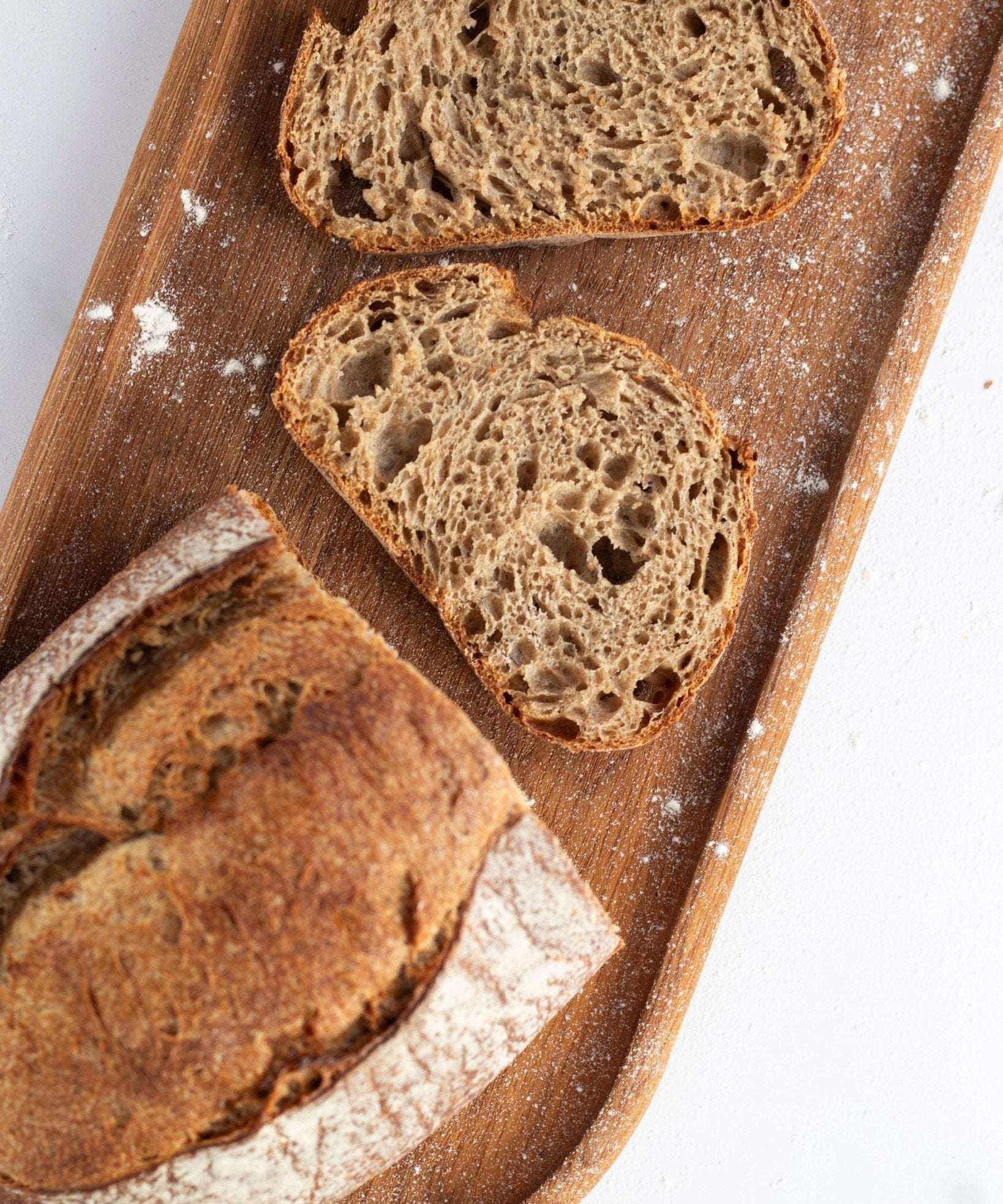 Tranches de pain de campagne artisanal sur une planche en bois avec farine.