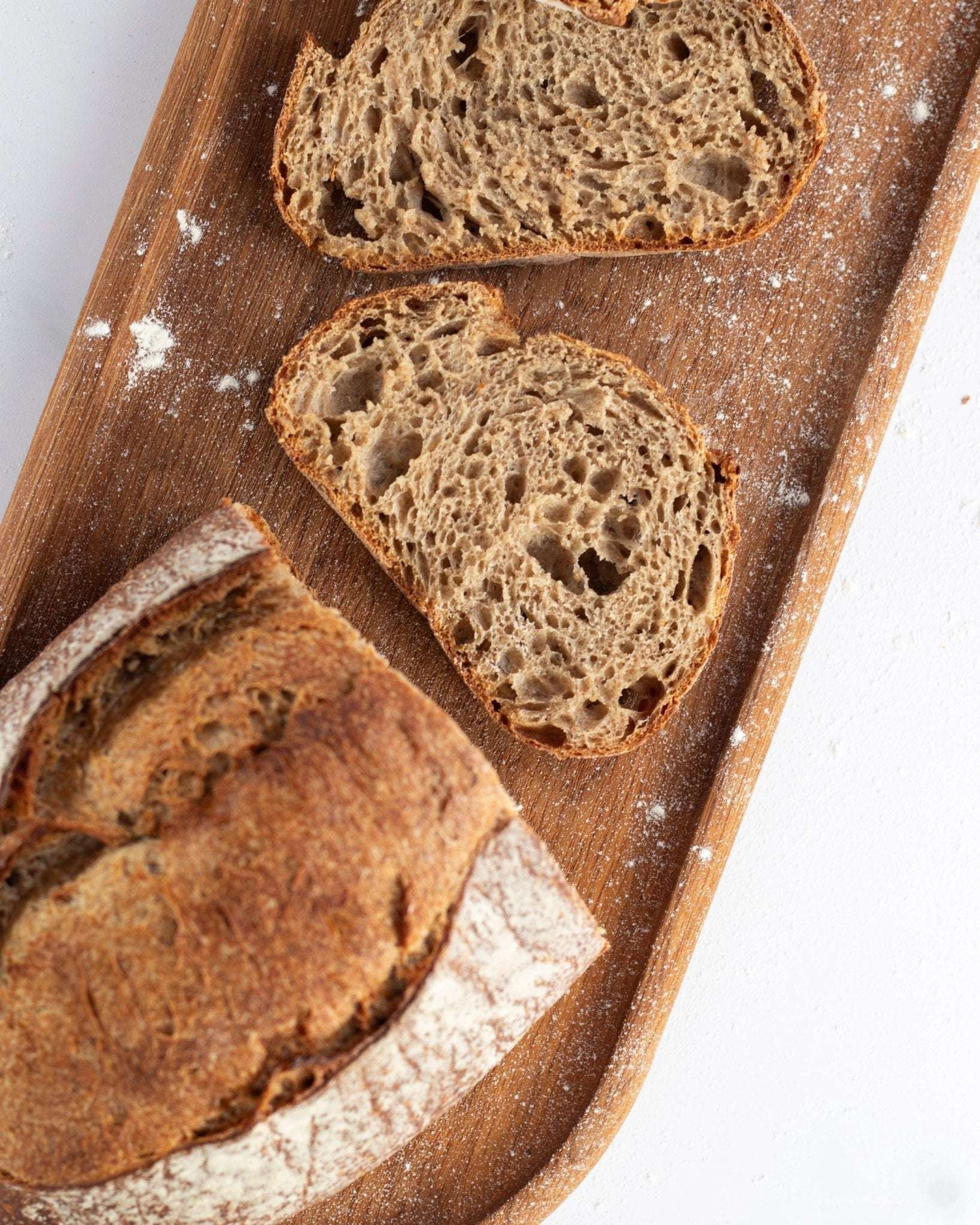 Tranches de pain de campagne artisanal sur une planche en bois avec farine.