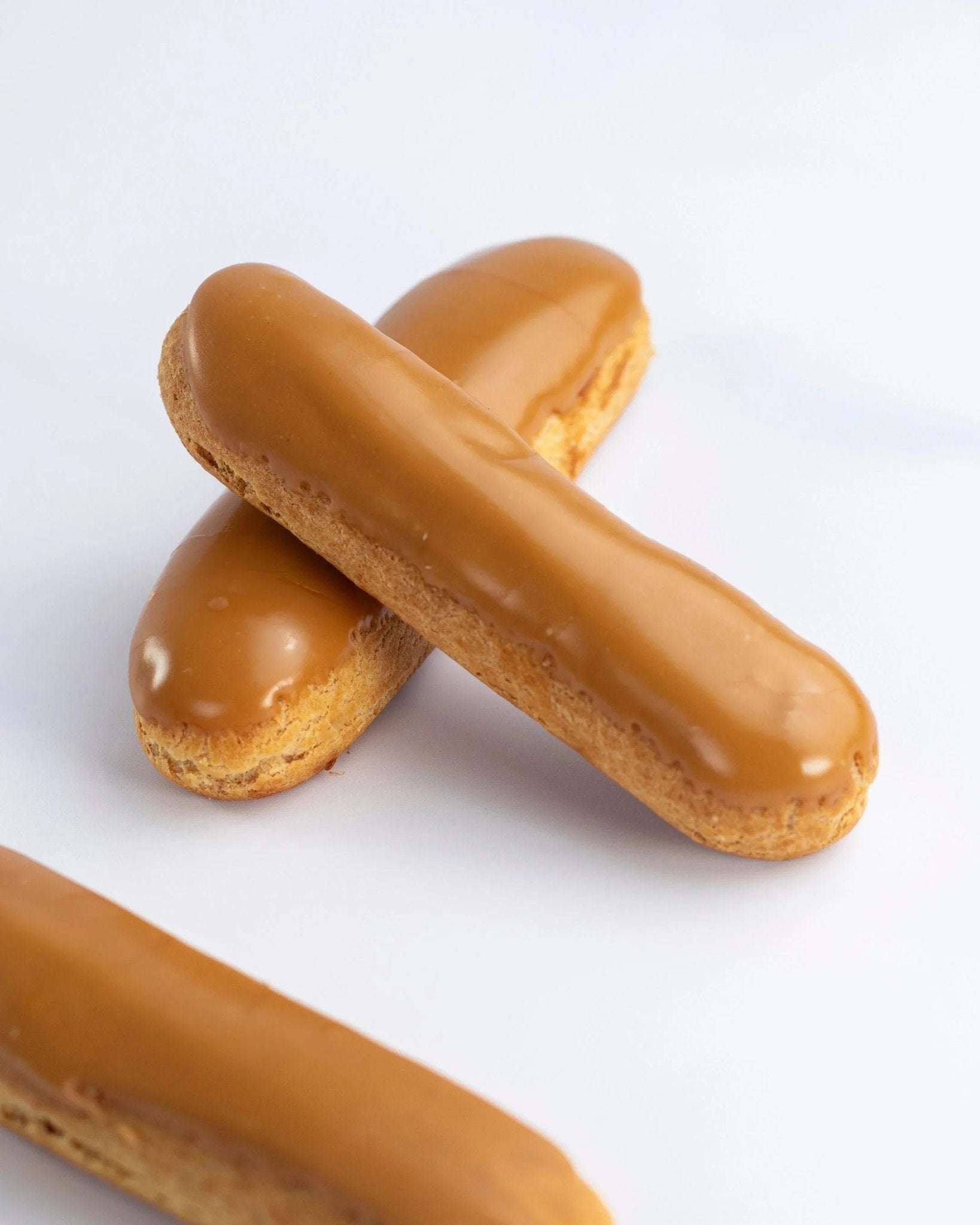 Deux éclairs au café Maison Vatelier avec un glaçage brillant sur fond blanc.