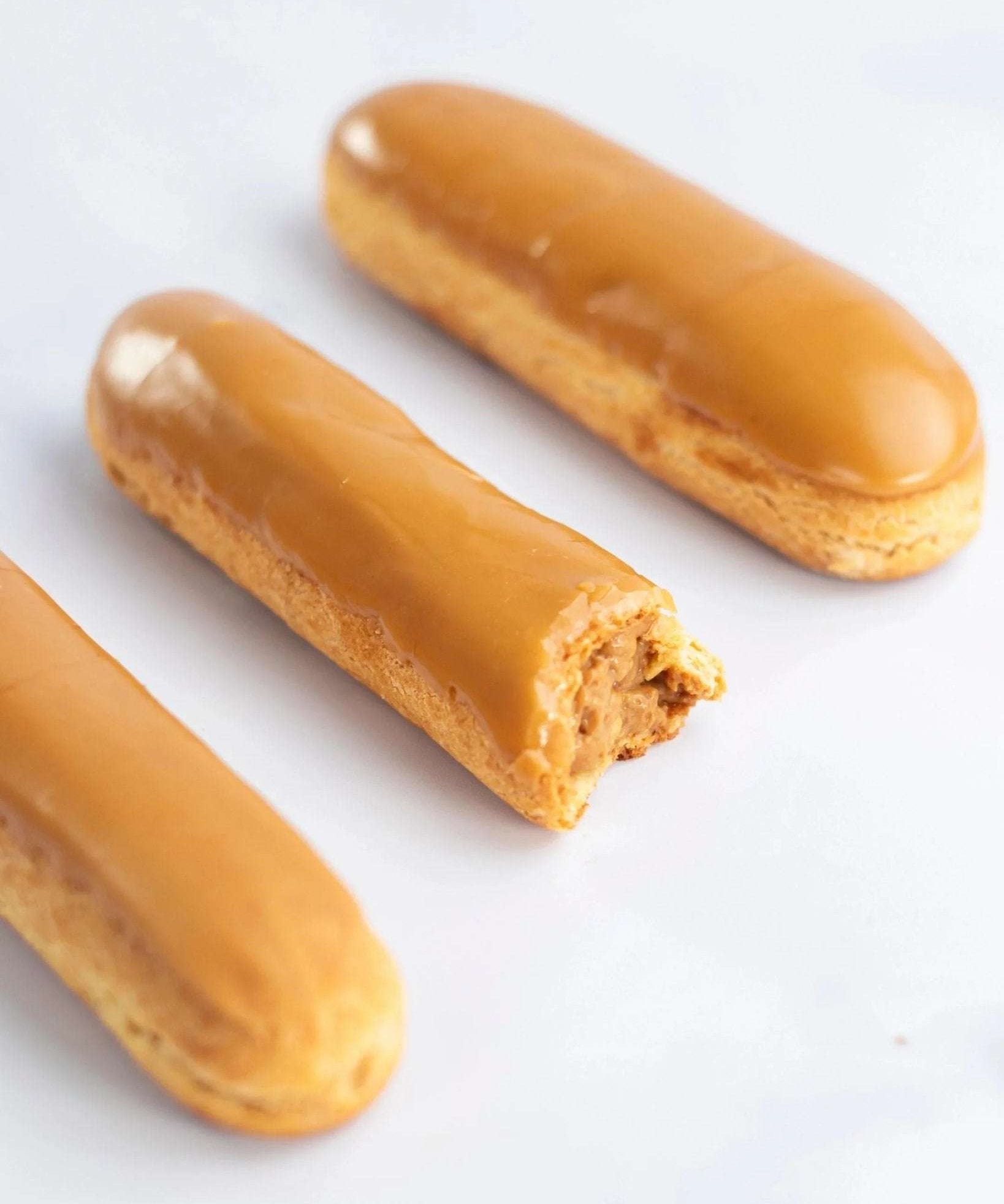 Trois éclairs au café Maison Vatelier avec glaçage caramel, l'un étant entamé.