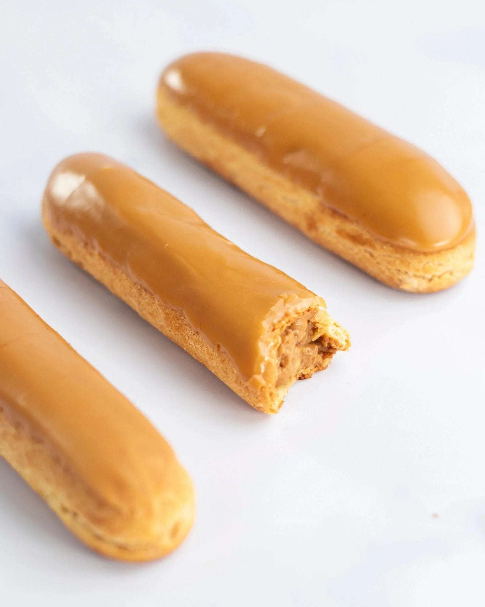 Trois éclairs au café Maison Vatelier avec glaçage caramel, l'un étant entamé.