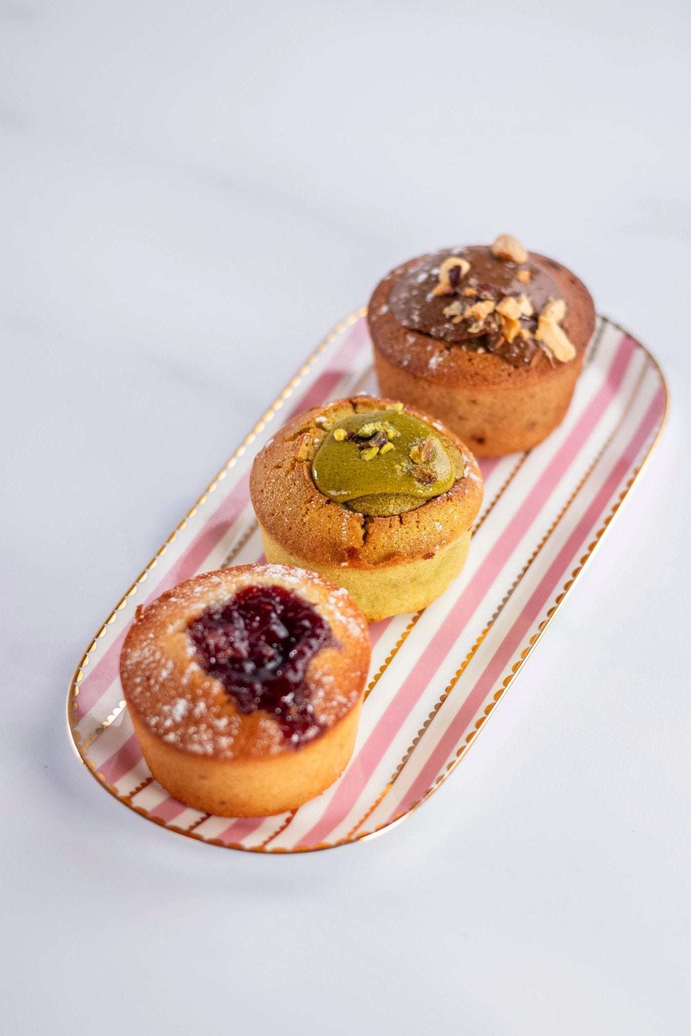 Assortiment de trois financiers Maison Vatelier, dont un à la pistache, sur un plateau rayé.