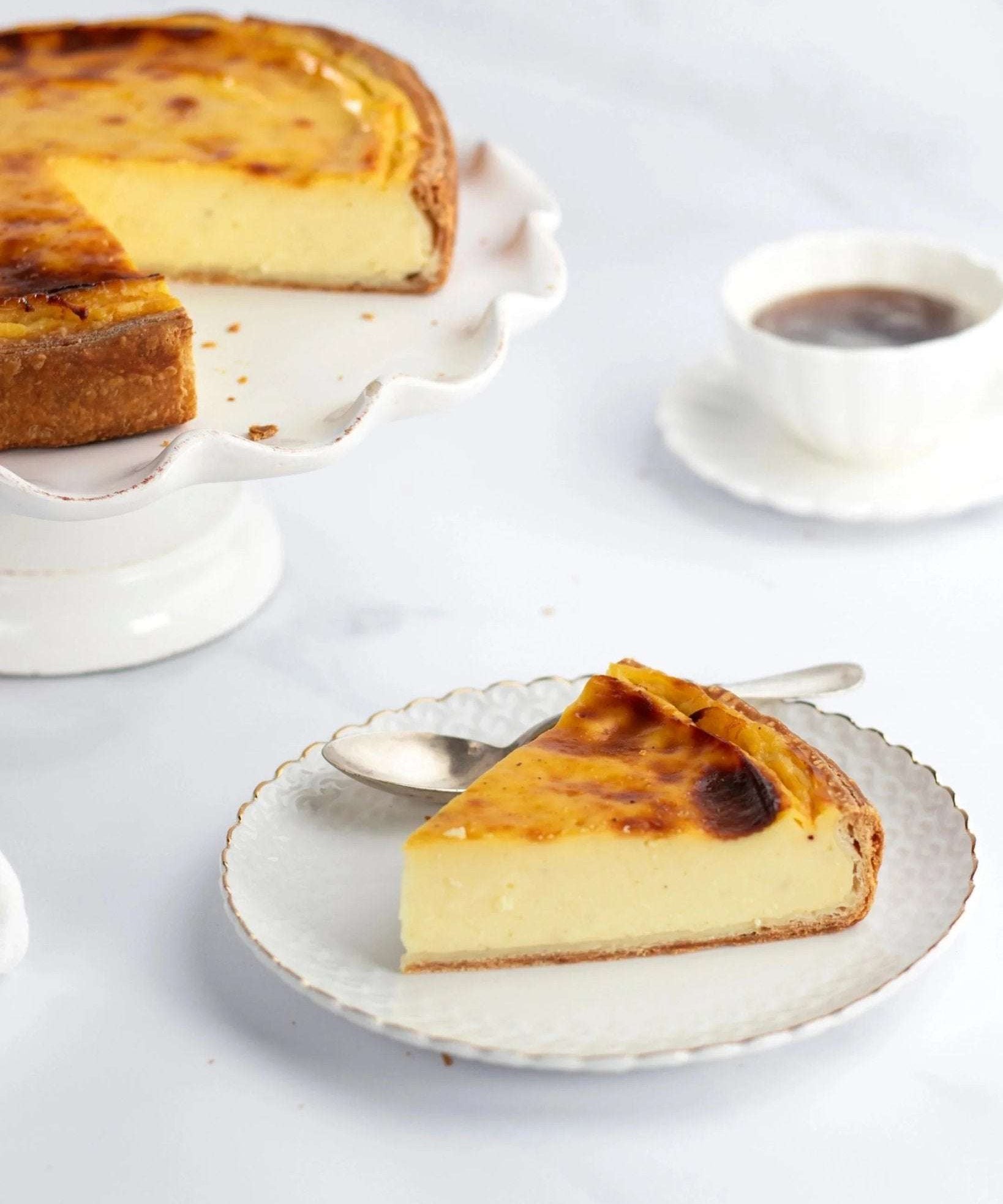 Part de flan vanille Maison Vatelier sur une assiette blanche avec le gâteau entier en arrière-plan.