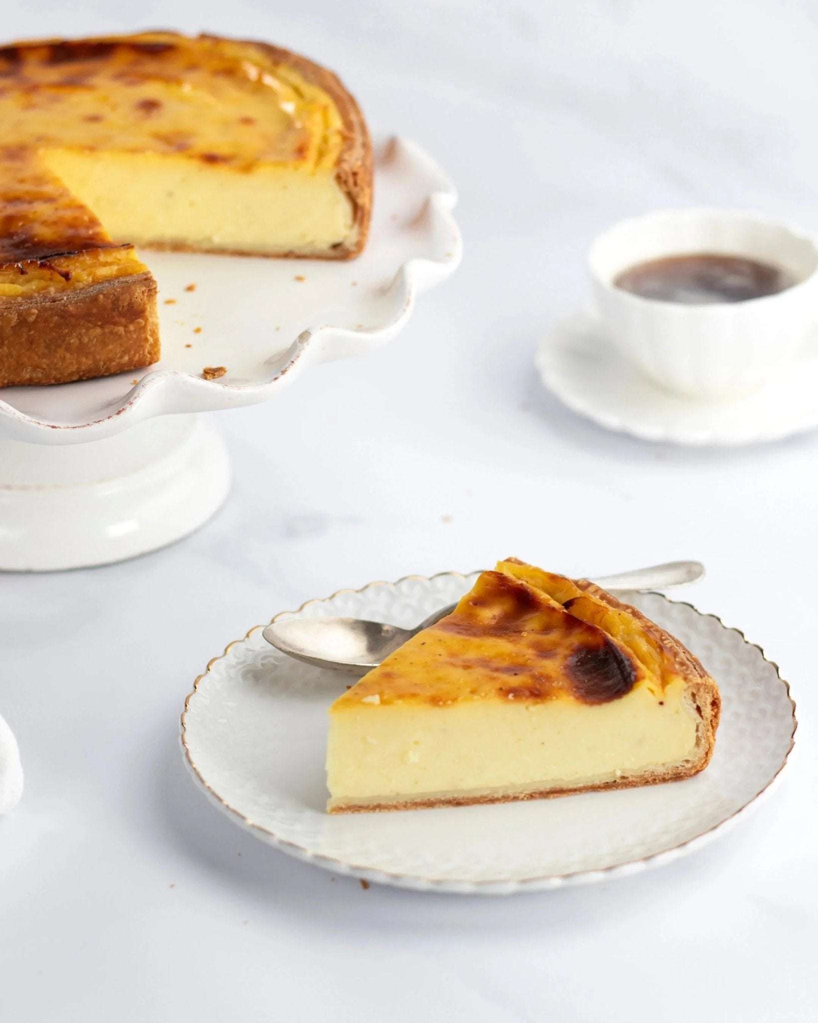 Part de flan vanille Maison Vatelier sur une assiette blanche avec le gâteau entier en arrière-plan.