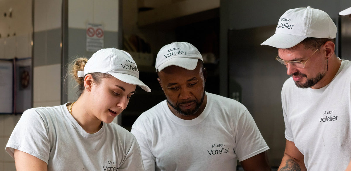 Trois pâtissiers de la Maison Vatelier en tenue blanche travaillant en cuisine.