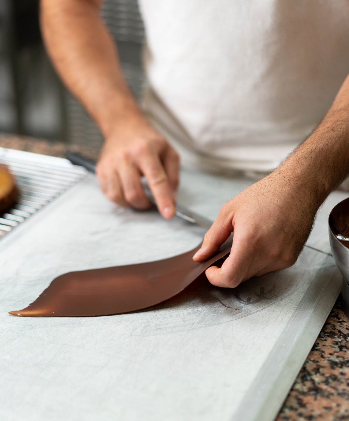 Pâtissier façonnant une fine plaque de chocolat sur un plan de travail.