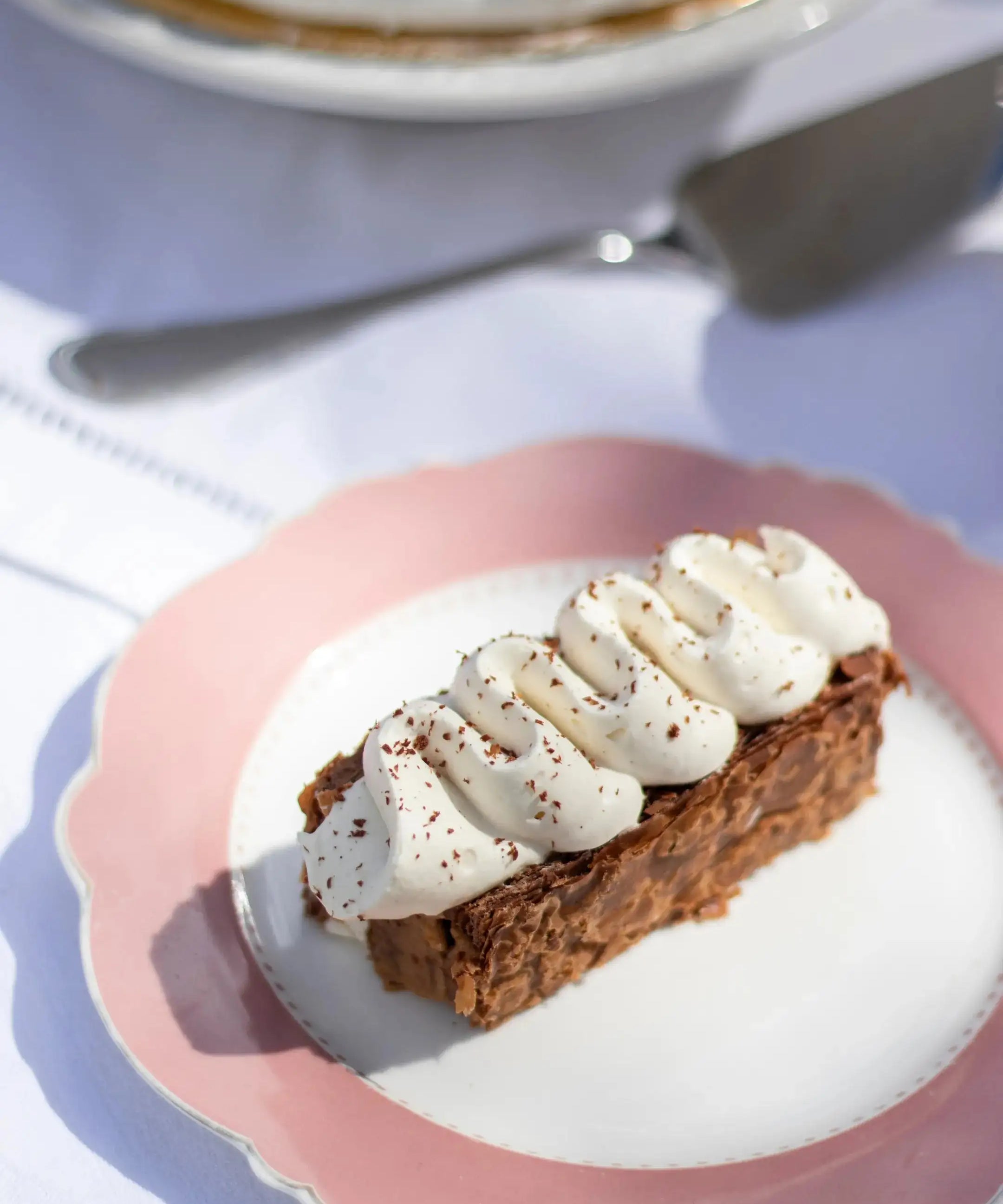 Part de Mille-Feuille praliné tonka Maison Vatelier avec crème chantilly sur assiette rose