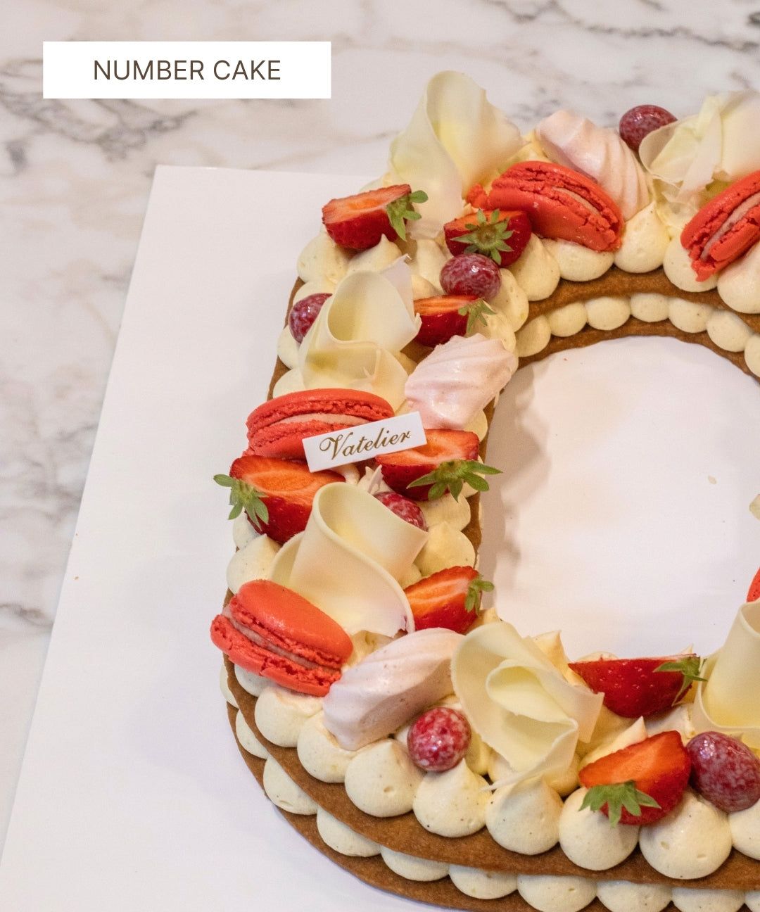Gâteau chiffre décoré de macarons rouges, fraises fraîches, meringue et chocolat blanc.