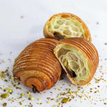 Pain au chocolat à la pistache Maison Vatelier coupé en deux et saupoudré d'éclats de pistaches.