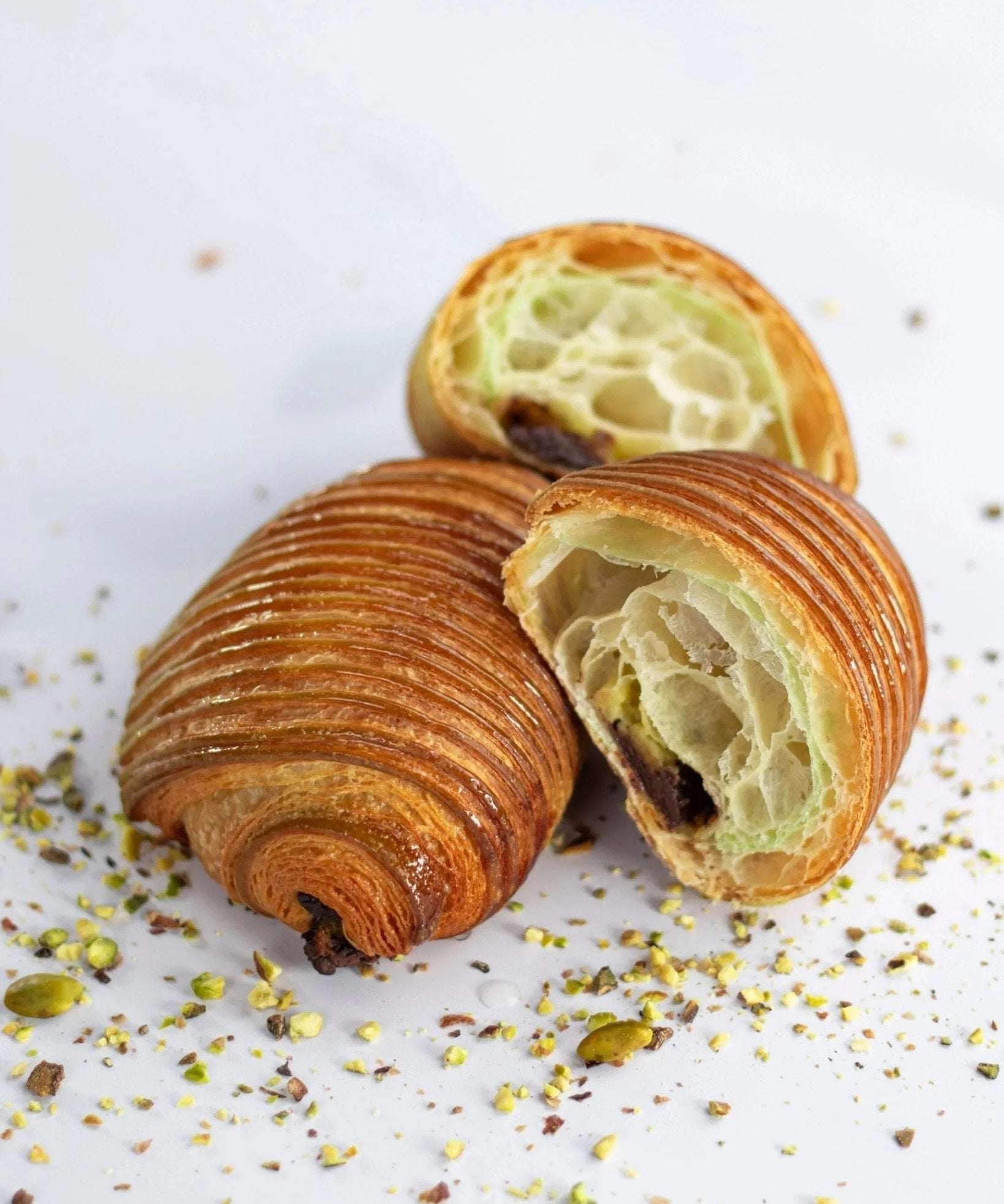 Pain au chocolat à la pistache Maison Vatelier coupé en deux et saupoudré d'éclats de pistaches.