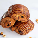 Trois pains au chocolat praliné Maison Vatelier croustillants et dorés sur fond blanc.