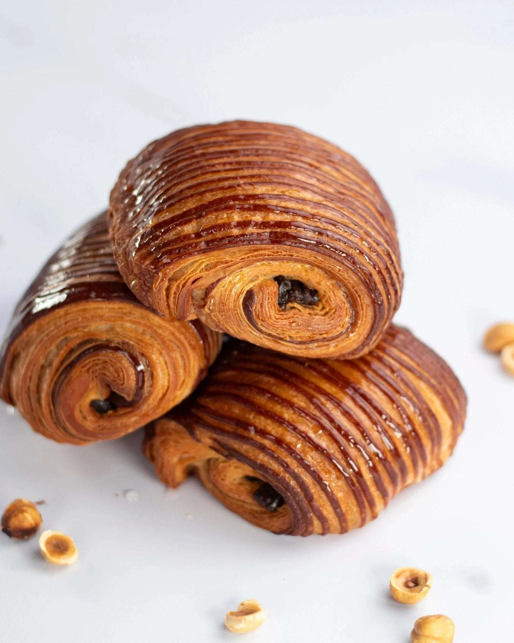 Trois pains au chocolat praliné Maison Vatelier croustillants et dorés sur fond blanc.