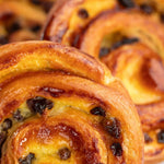 Gros plan de pains raisins Maison Vatelier, viennoiseries dorées et brillantes avec raisins secs.