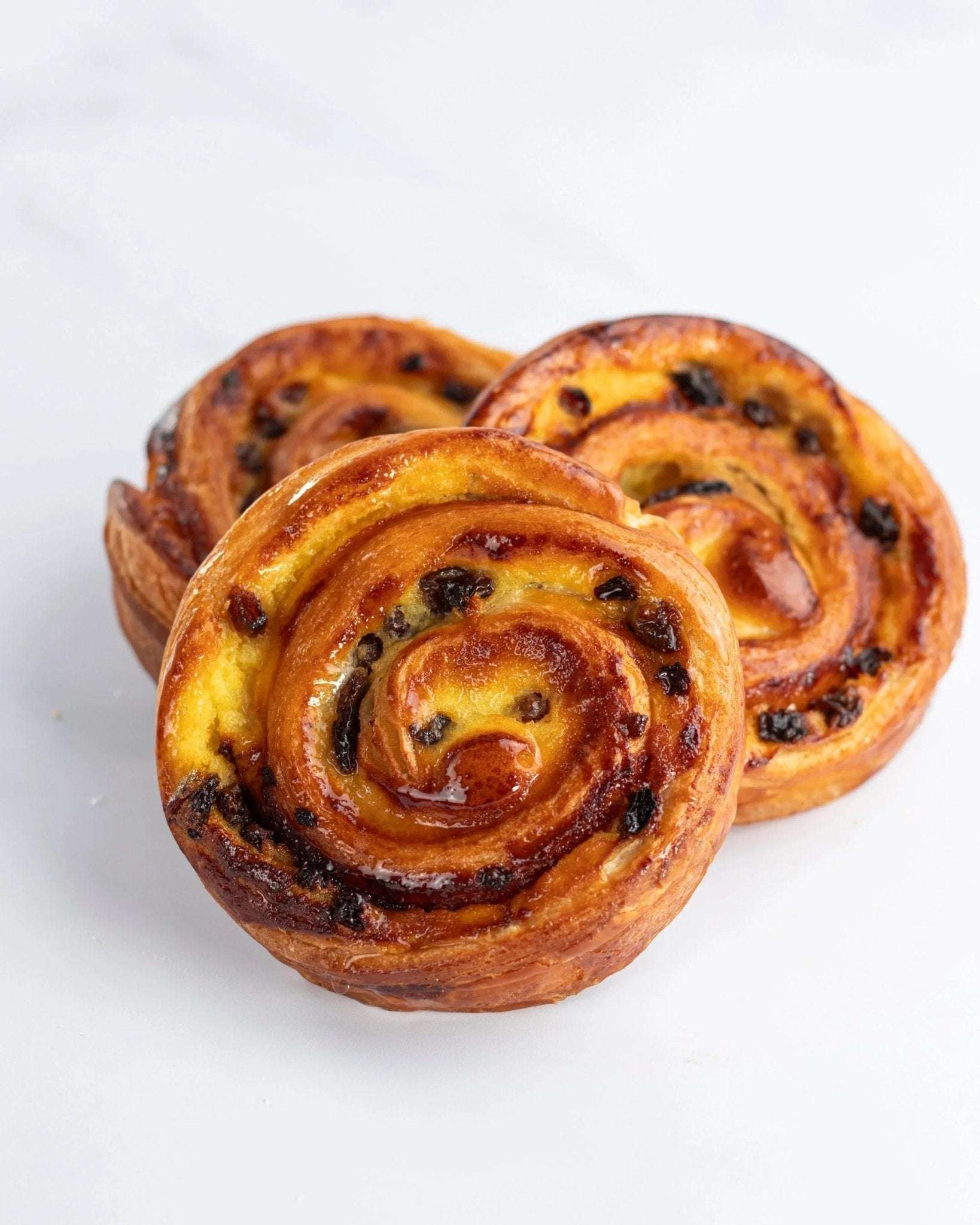 Trois pains aux raisins Maison Vatelier dorés et gourmands sur fond blanc.