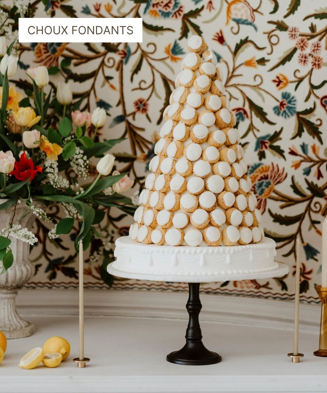Pièce montée de choux fondants sur un support blanc devant un papier peint floral.