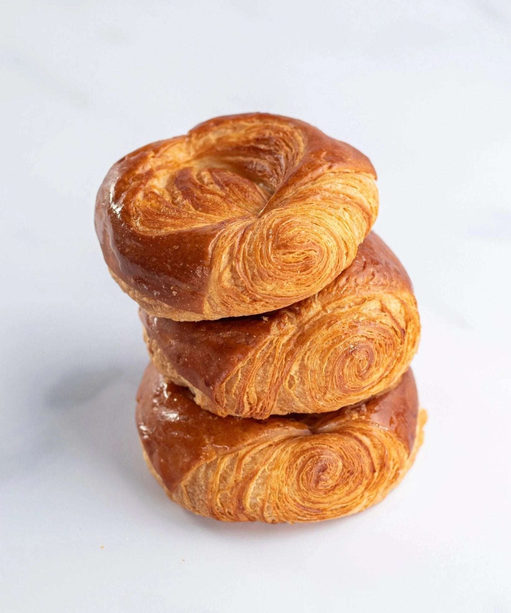 Pile de trois roulettes feuilletées dorées Maison Vatelier sur fond blanc.