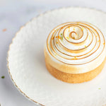 Pâtisserie individuelle avec meringue italienne brûlée en spirale sur une assiette blanche.