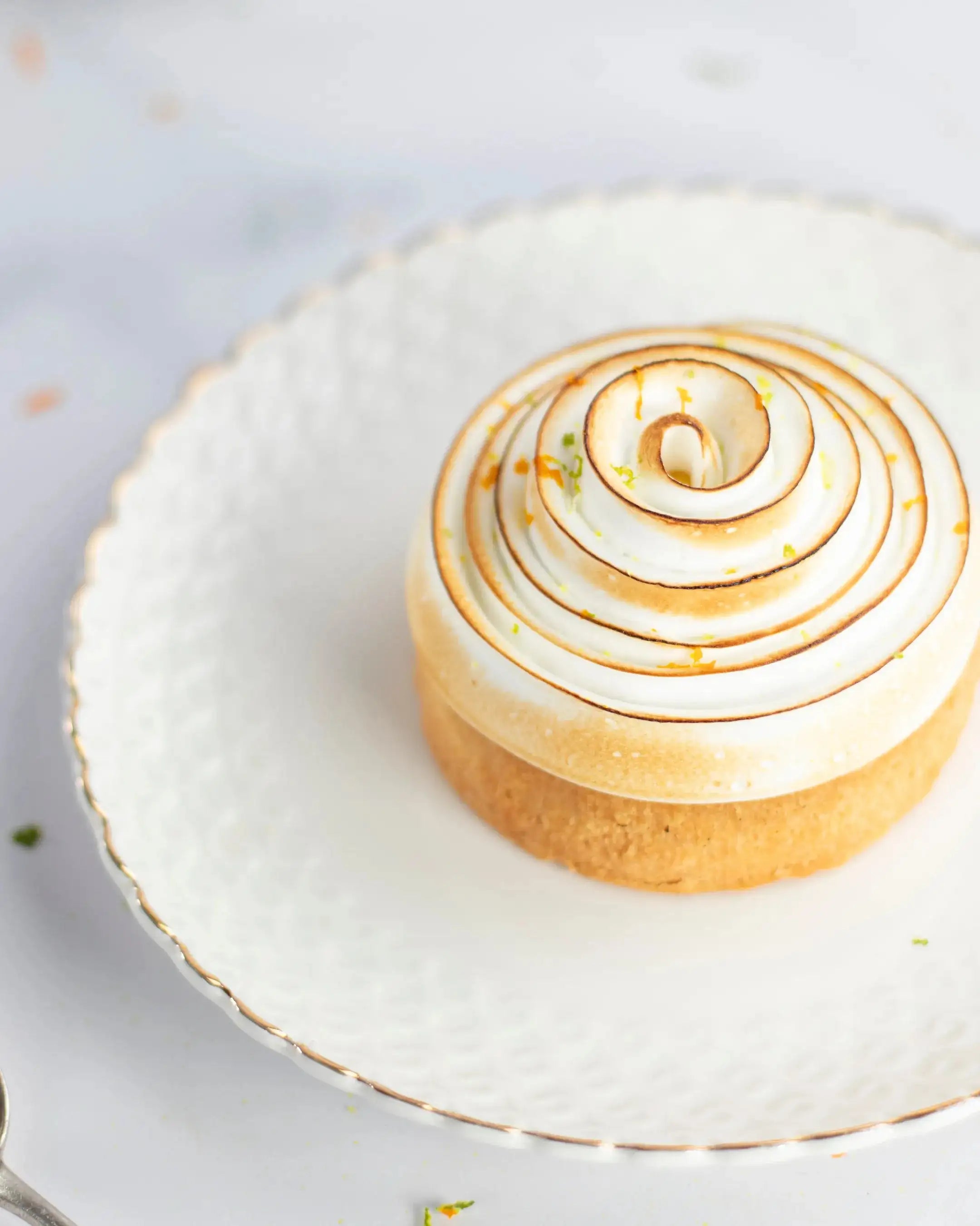 Pâtisserie individuelle avec meringue italienne brûlée en spirale sur une assiette blanche.