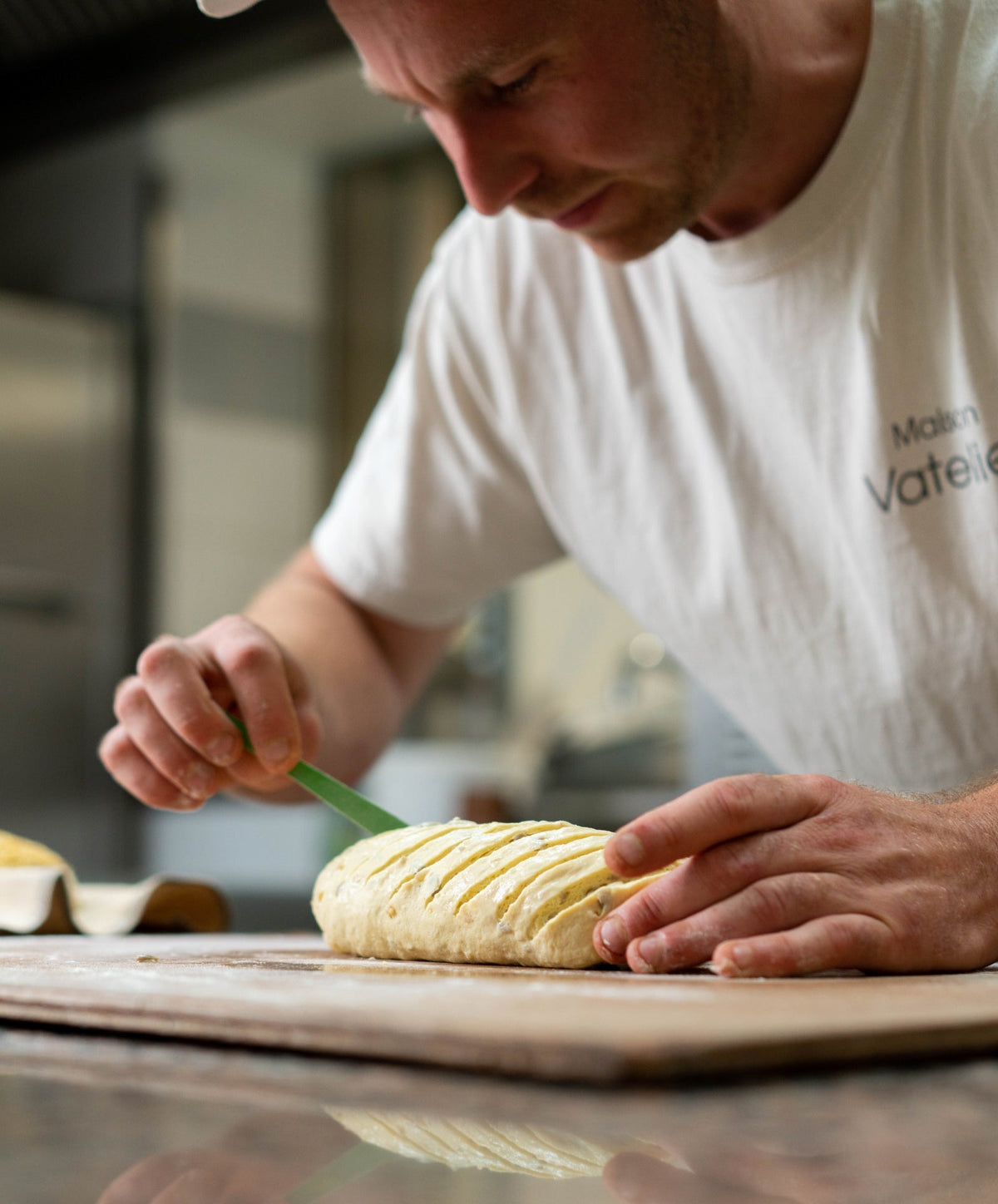 Un boulanger façonnant et scarifiant un pâton de pain sur un plan de travail.