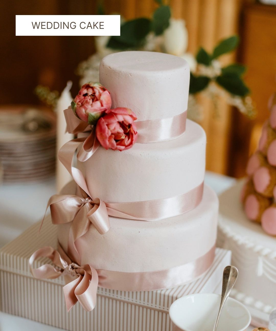 Pièce montée de mariage à trois étages rose pâle avec rubans et fleurs fraîches.